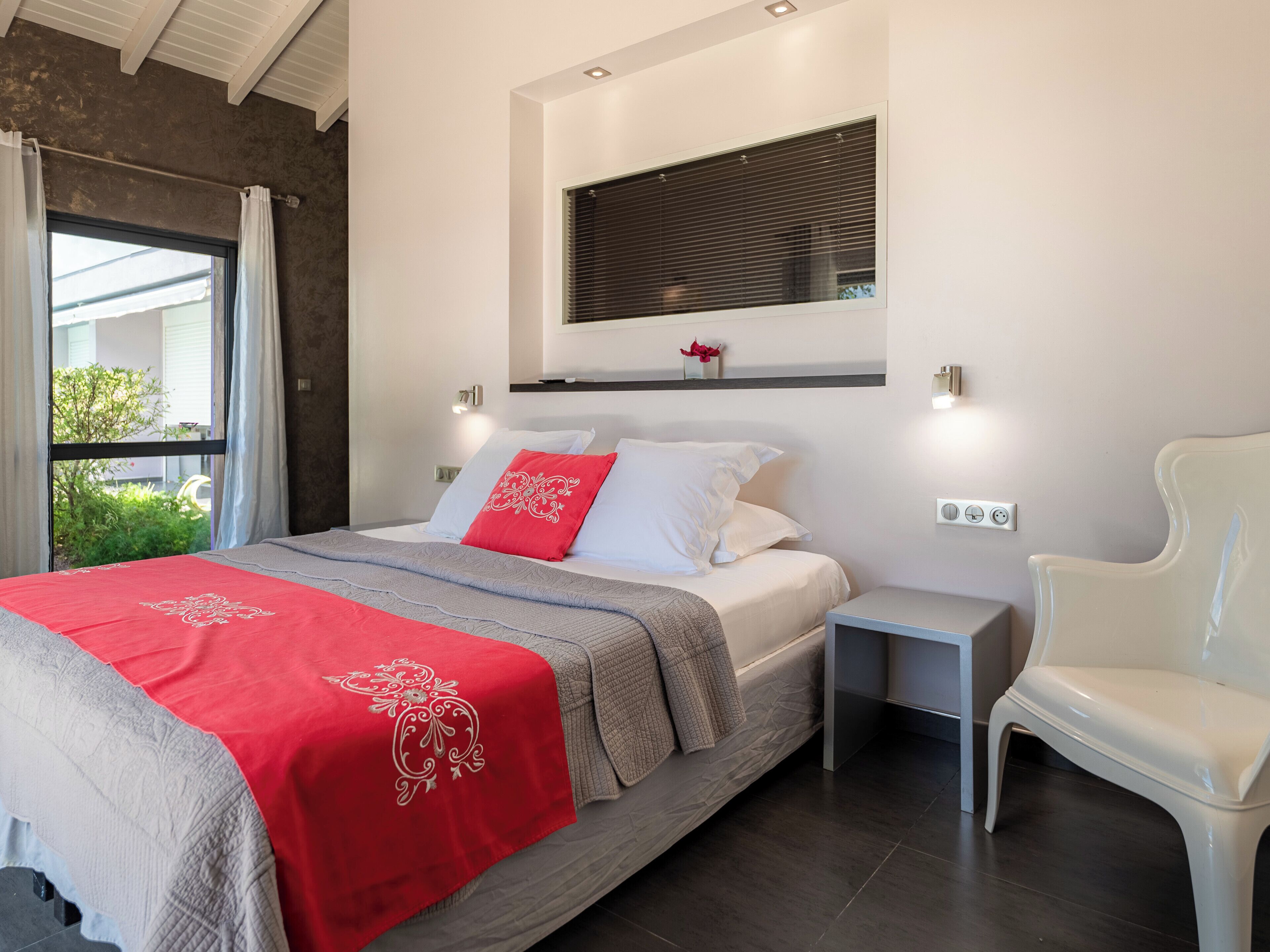 Ein modernes Schlafzimmer mit Bett, Nachttischen, einem Sessel und einem Fenster mit Jalousien.