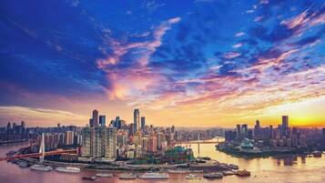 A city skyline at sunset with high-rise buildings and a river.