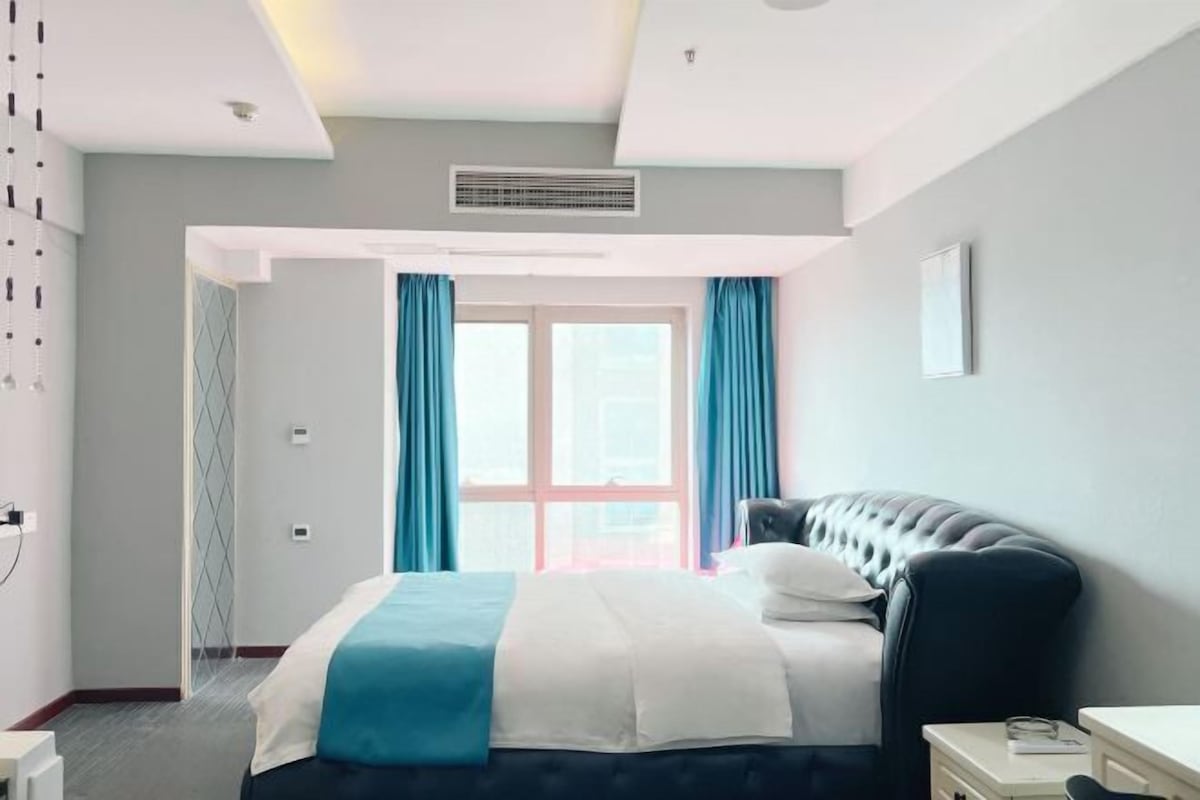 A modern hotel room with a large bed, a desk, and a window with curtains.