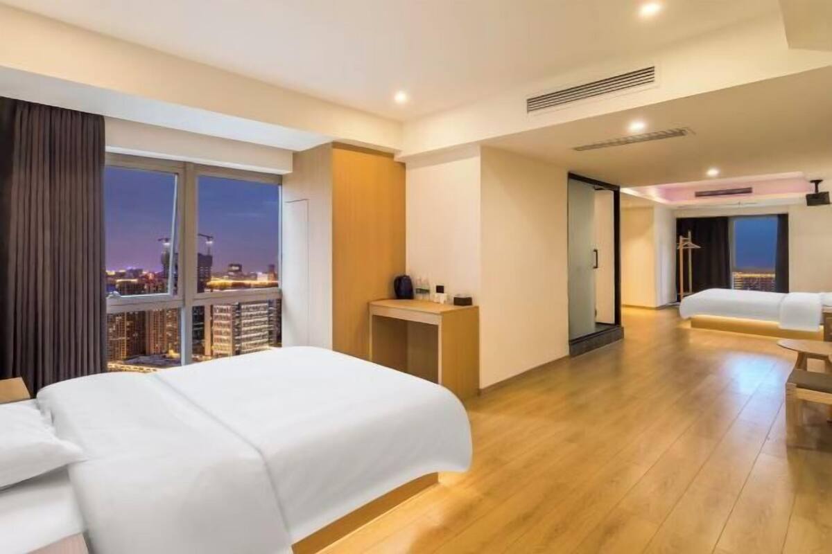 A modern hotel room with a large bed, a desk, and a view of the cityscape at night.