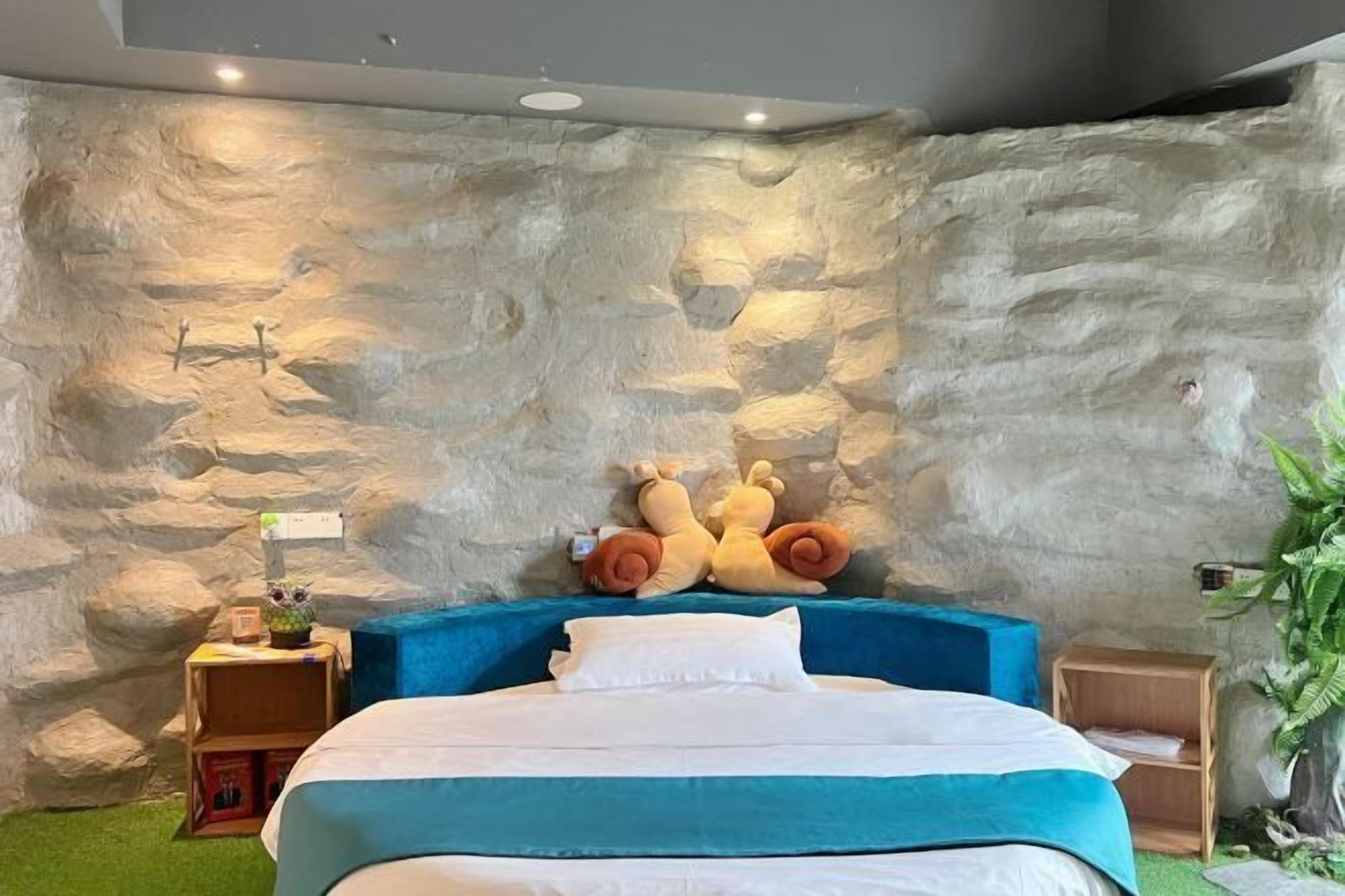A bedroom with a stone wall, a bed with a blue headboard, and two plush toys on the wall.