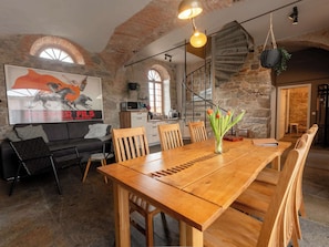 Un grand espace à manger avec une table et des chaises en bois, un canapé noir et une cuisine en arrière-plan.