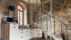 A kitchen with white cabinets, a stone wall, a wooden counter, and a metal staircase. - Duplex flat with a fireplace in a historic vaulted building (Großharthau)