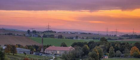 Un paysage rural caractérisé par un bâtiment imposant, de vastes champs ouverts et des lignes électriques qui disparaissent à l’horizon.