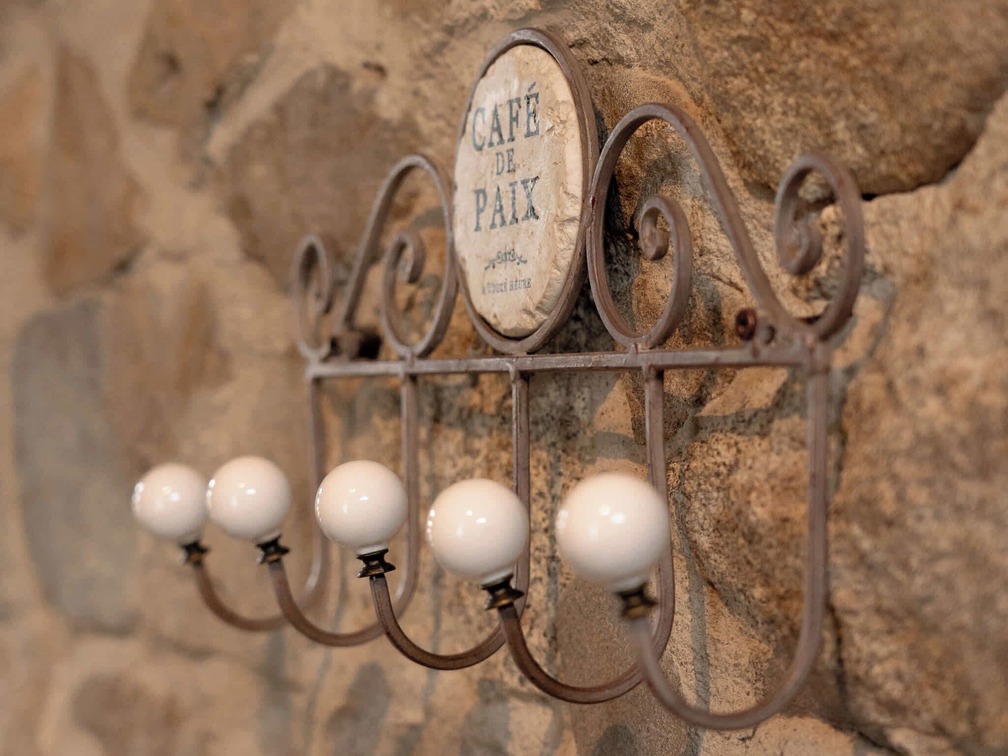 Un estante metálico de pared con un letrero que dice 'CAFÉ DE PAIX' y cinco objetos esféricos blancos colgando de él.