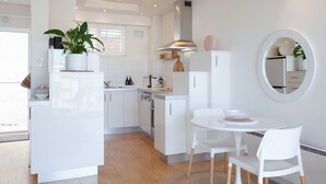 A modern kitchen with white cabinetry, a dining area with a round table and chairs, and a large mirror on the wall. - Harbour the Sun, McMahons Point Isyd (McMahons Point)