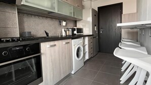 Eine moderne Küche mit Herd, Backofen, Mikrowelle und Waschmaschine. Ein Essbereich mit weißen Stühlen und einem Tisch ist ebenfalls vorhanden.