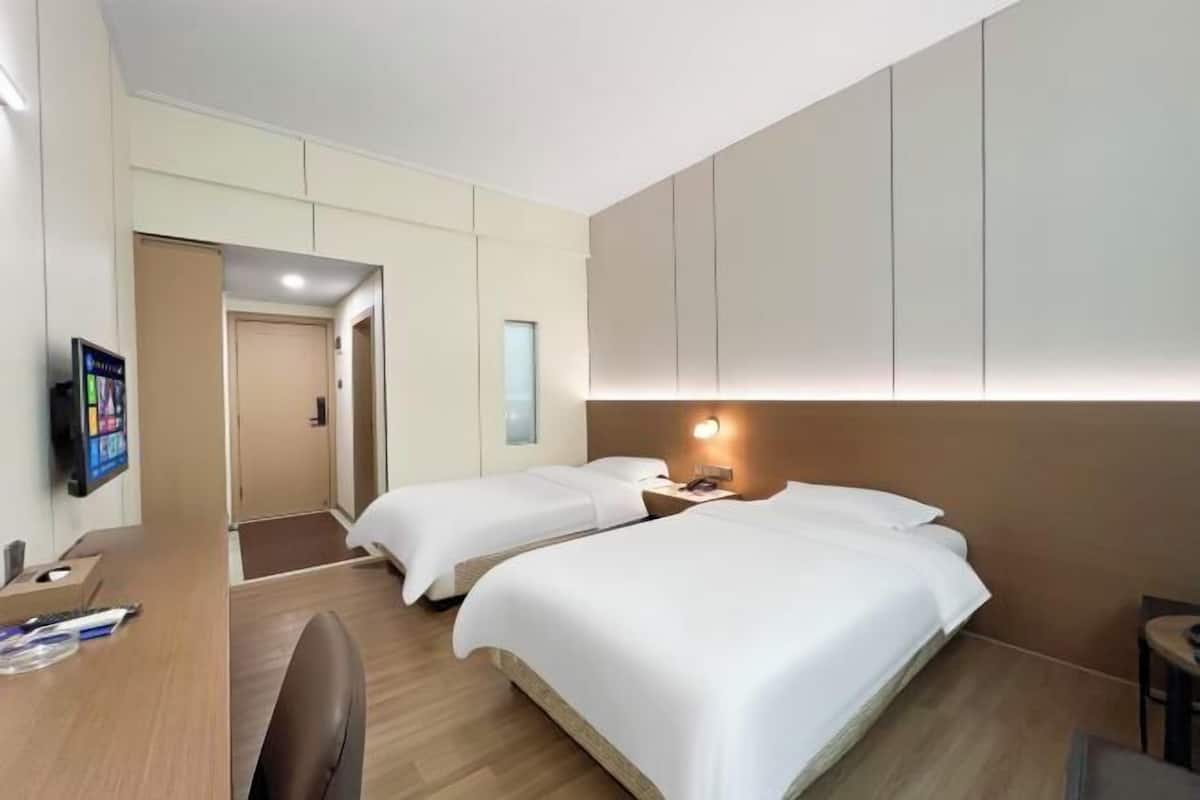 A hotel room with two beds, a desk, a TV, and a small table.