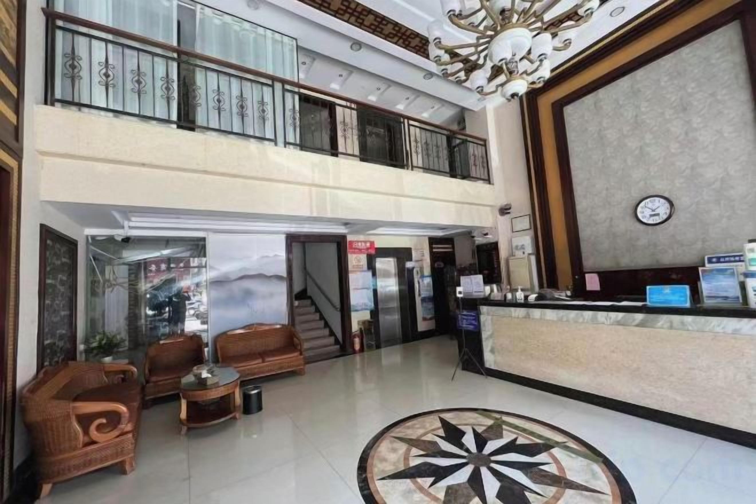 A hotel lobby with a reception desk, seating area, and a staircase leading to the upper floor.
