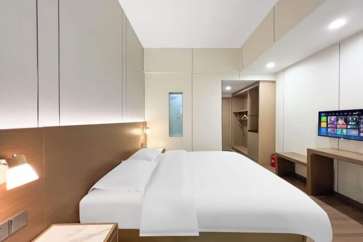 A modern hotel room with a large bed, a bedside table, a TV, and a wardrobe.