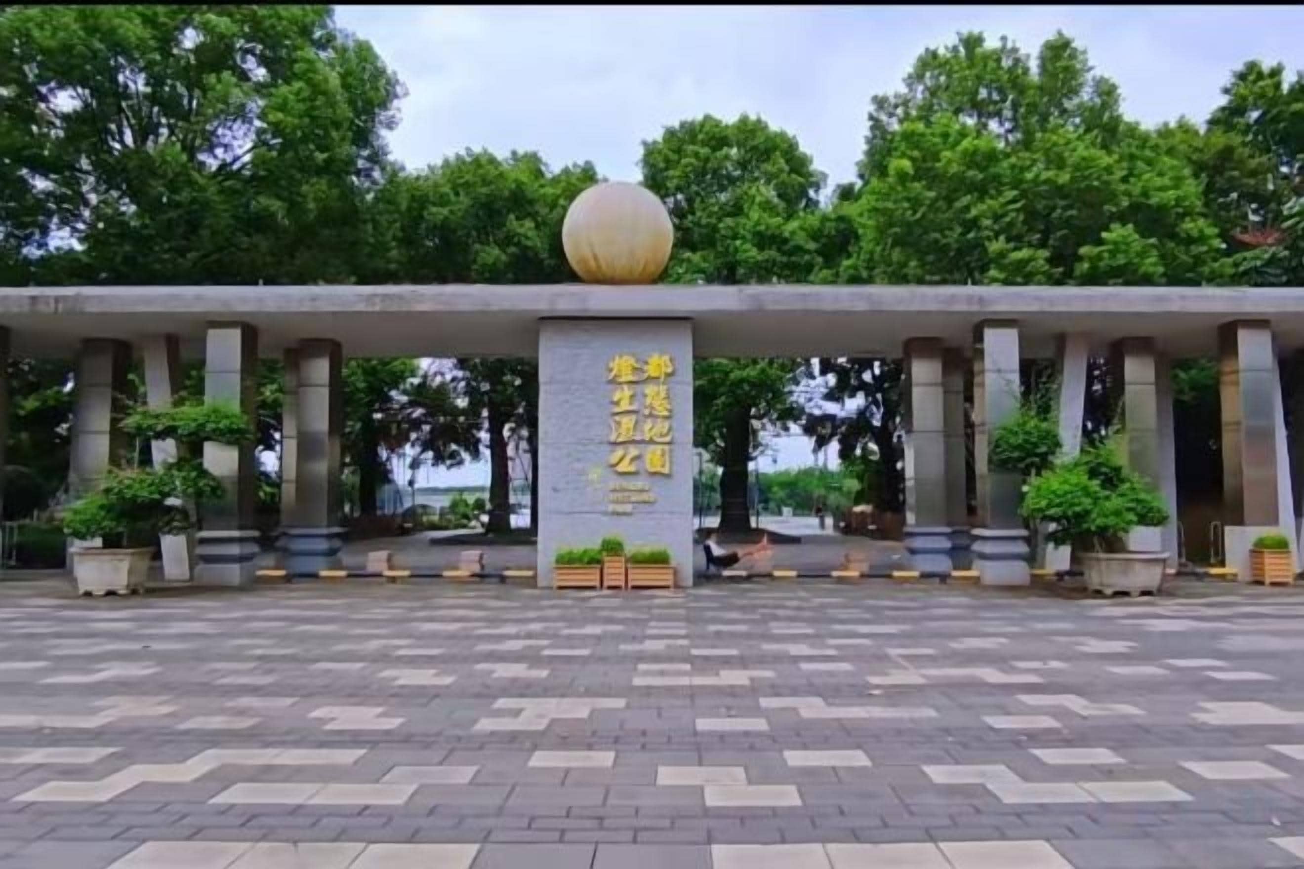 A building entrance with a large spherical object on top, columns, and a paved area with potted plants.