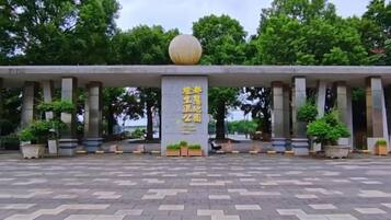A building entrance with a large spherical object on top, columns, and a paved area with potted plants.