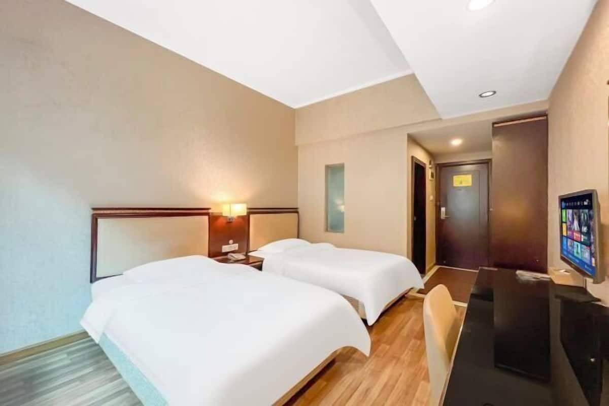 A hotel room with two beds, a desk, a television, and a door.