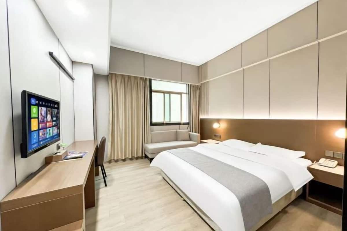 A modern hotel room with a bed, a desk, a chair, a TV, and a window with curtains.