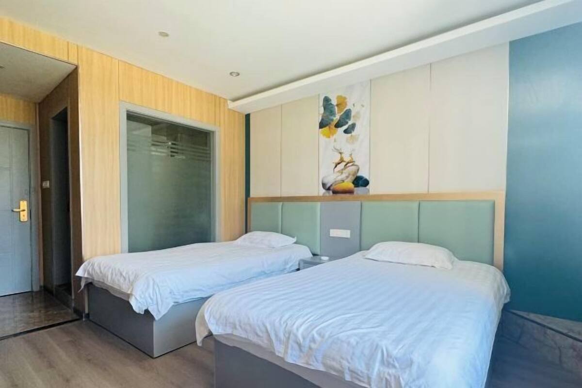 A hotel room with two beds, a wardrobe, a painting on the wall, and a door to the left.