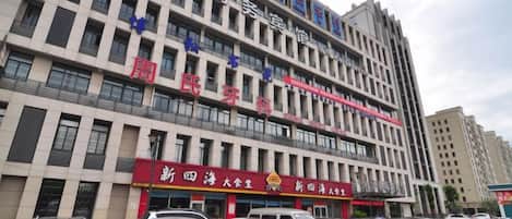 A multi-story building with several commercial establishments on the ground floor, including a restaurant and a bank. There are multiple parked cars in front of the building.