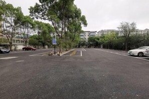 Un estacionamiento con espacios delimitados, árboles y edificios al fondo.