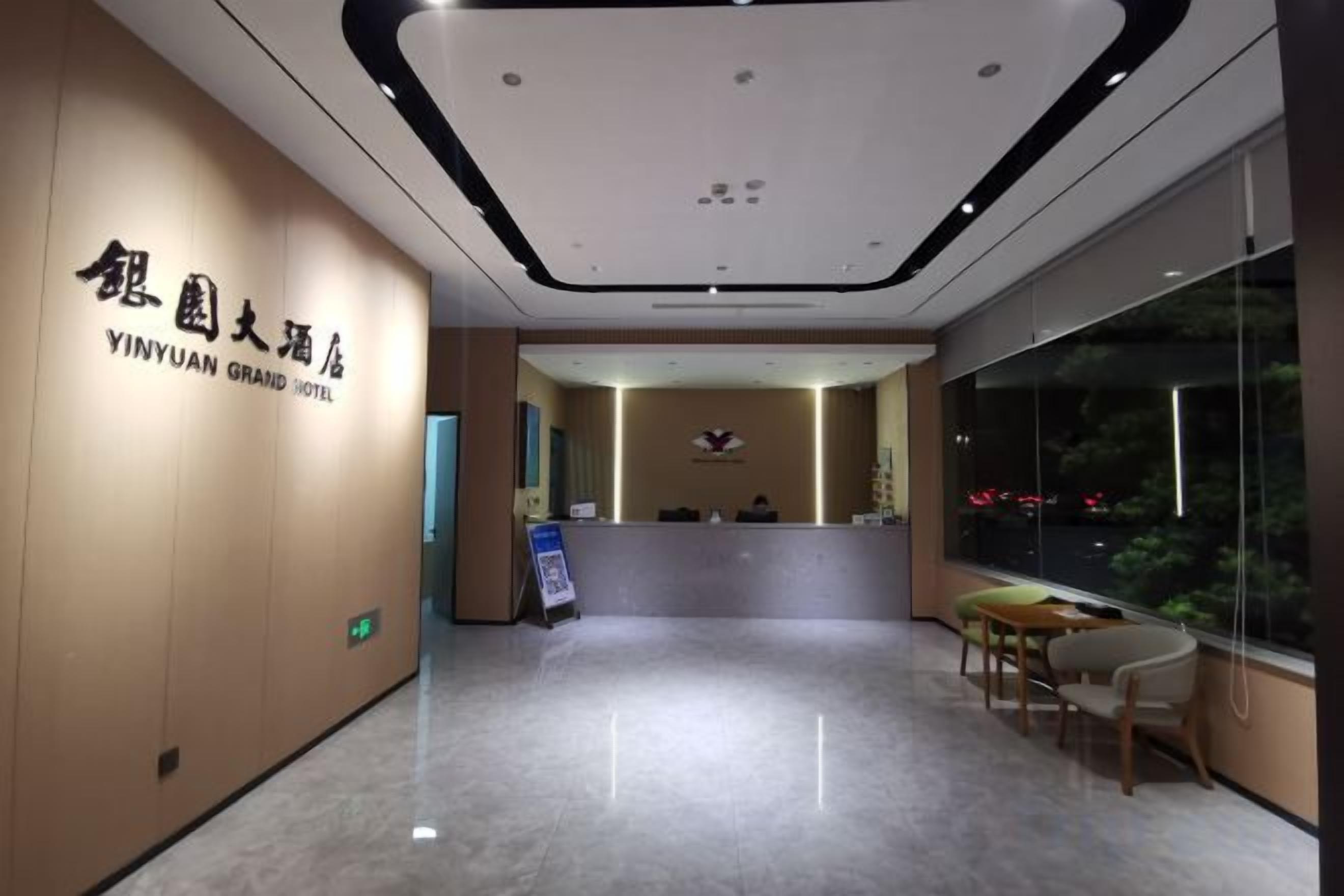 A hotel reception area with a reception desk, a seating area, and a large window providing a view of the outside.