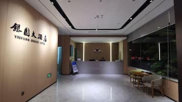 A hotel reception area with a reception desk, a seating area, and a large window providing a view of the outside.