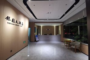 Zona de recepción de un hotel con mostrador, asientos y un amplio ventanal con vistas al exterior.