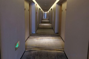 Pasillo de hotel con pisos alfombrados, puertas a ambos lados y una señal de salida verde.
