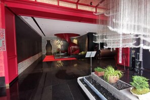 Un vestíbulo con una decoración en tonos rojo y negro, una recepción y una zona de estar con alfombra roja.