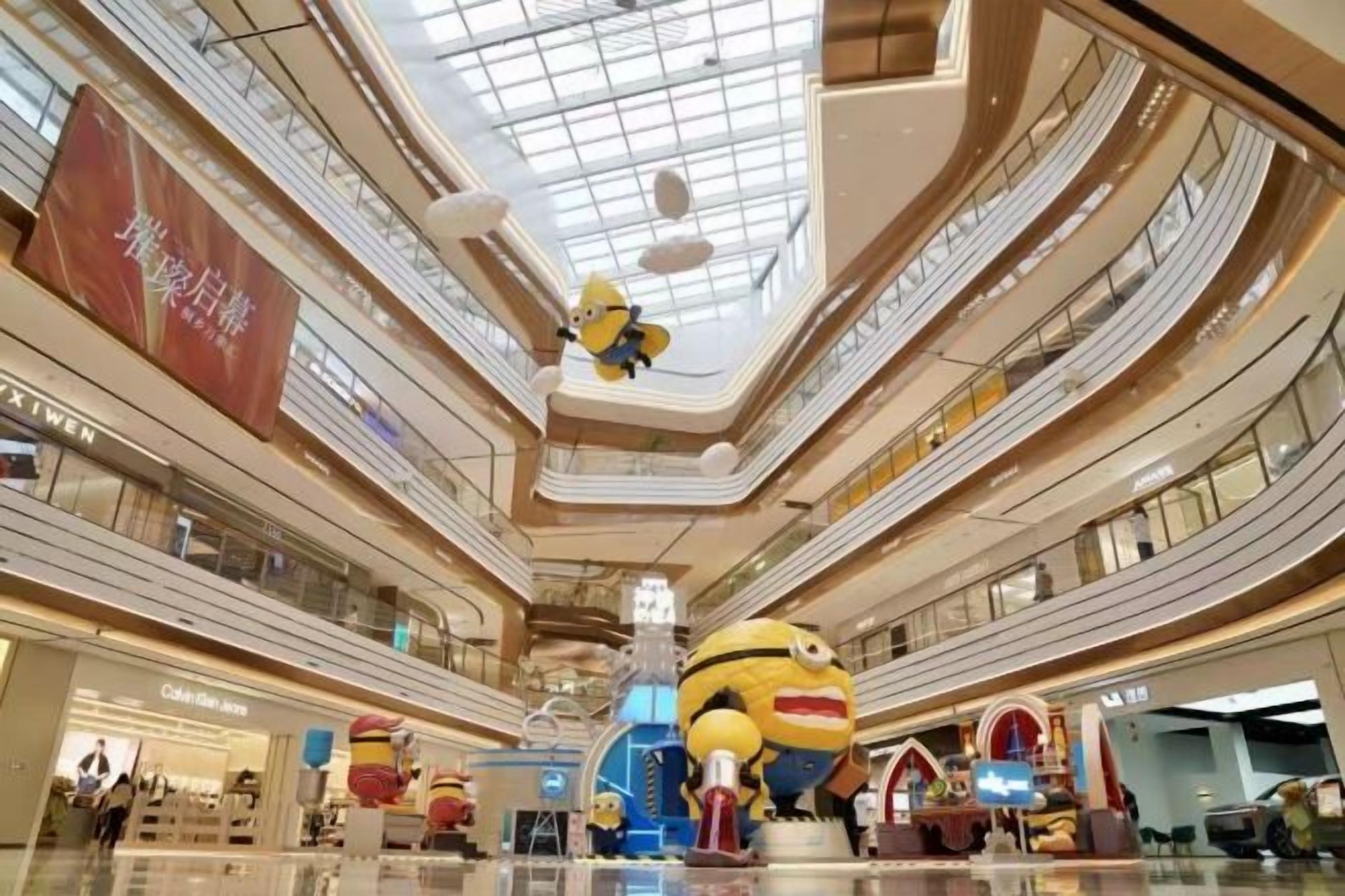 A multi-level shopping mall with a central atrium, escalators, and various retail stores.