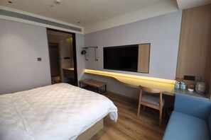 A modern hotel room with a bed, a desk, a chair, a TV mounted on the wall, and a small table. - Yinyuan Grand Hotel (Tongxiang)