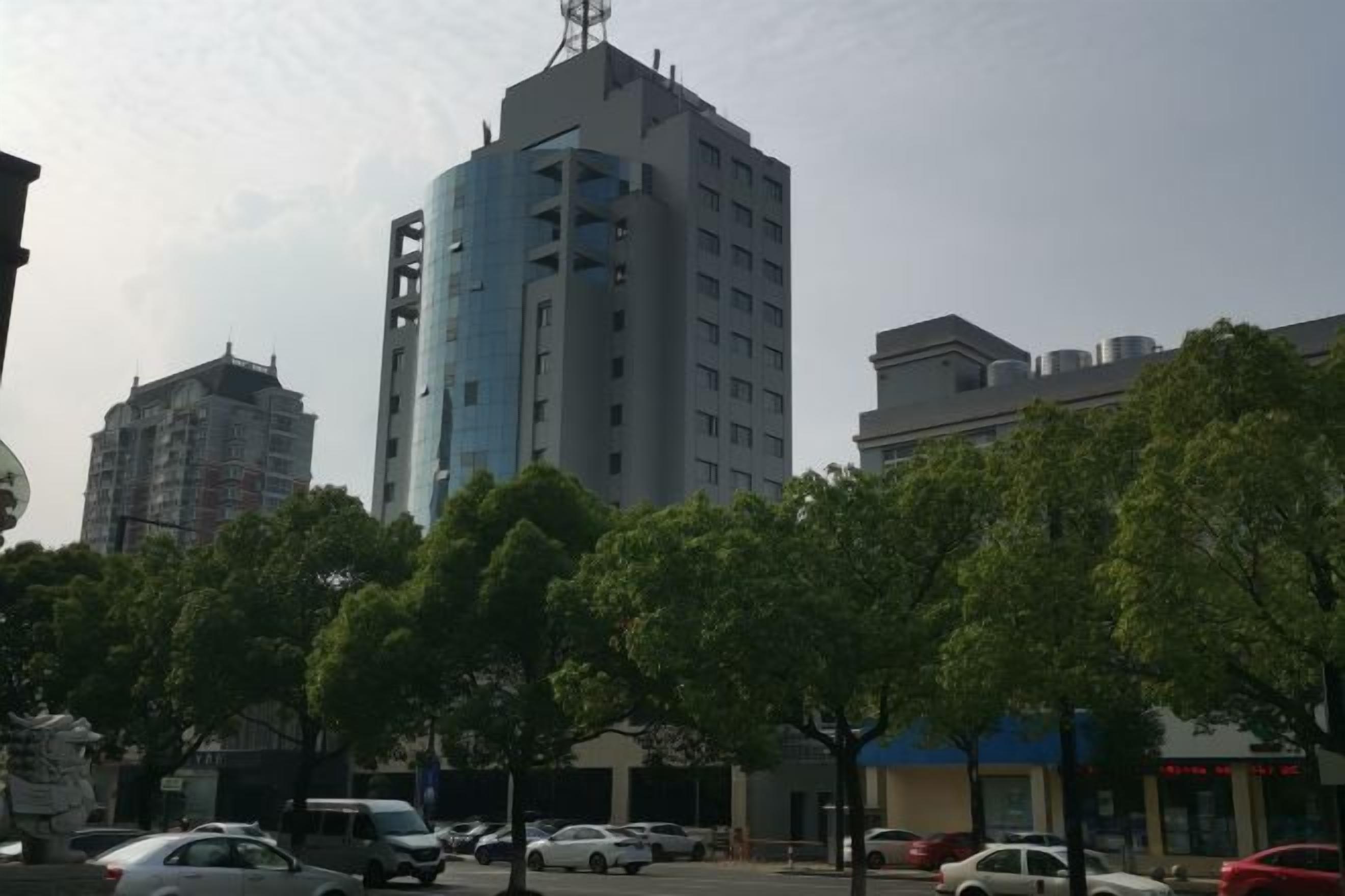 A multi-story building with a modern design, surrounded by trees and parked cars.