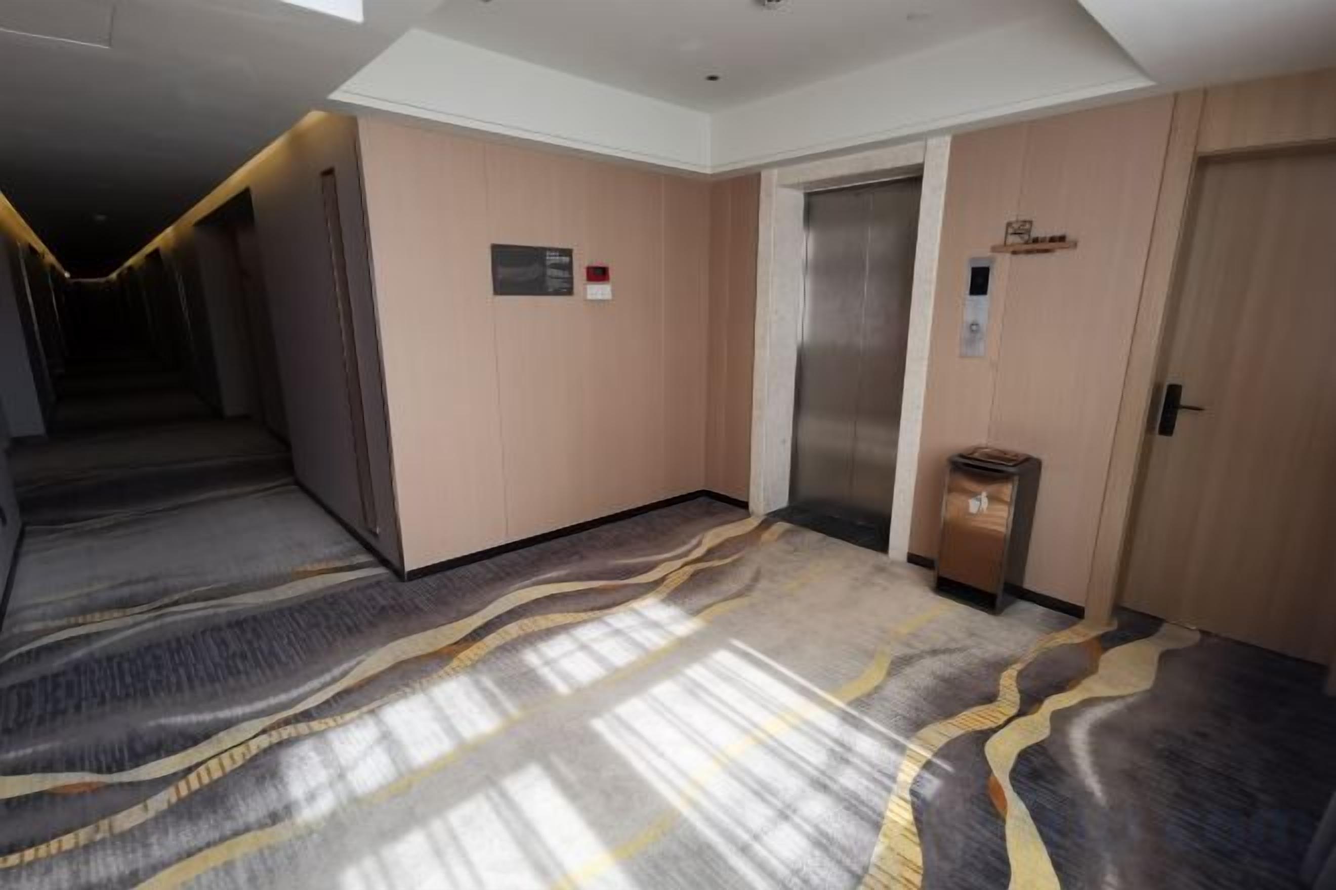A hotel corridor with an elevator, a trash bin, and a door.