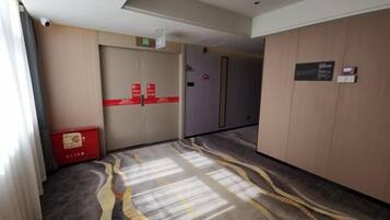 Un pasillo de hotel con piso alfombrado, una caja roja para almacenamiento y una puerta con un cartel.