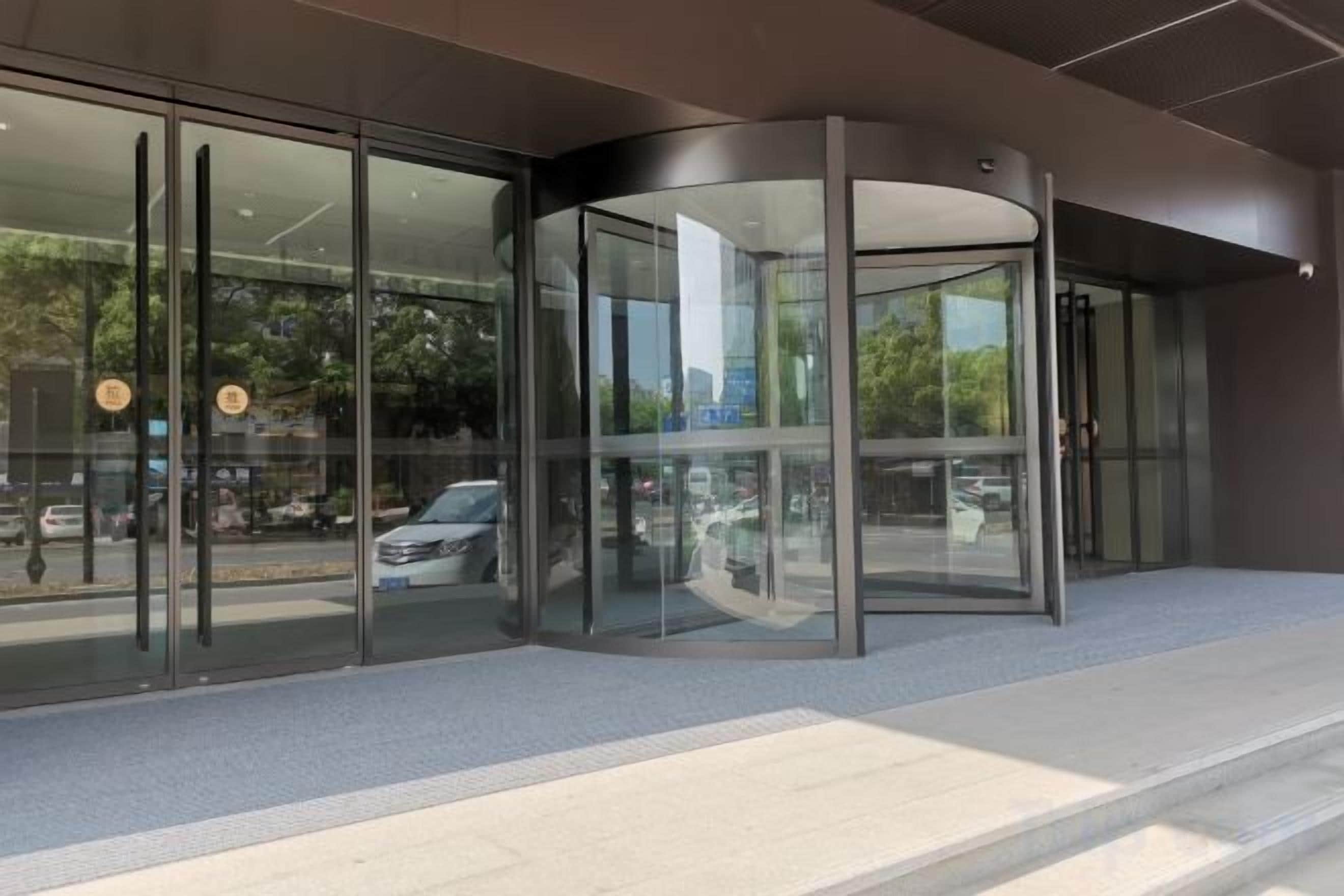 A modern building entrance with a revolving door, glass doors, and a paved area leading to the entrance.