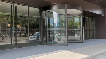 A modern building entrance with a revolving door, glass doors, and a paved area leading to the entrance.