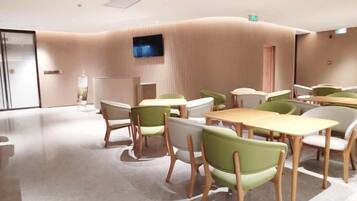 A modern conference room with tables and chairs, a flat-screen TV, and a curved wall design.