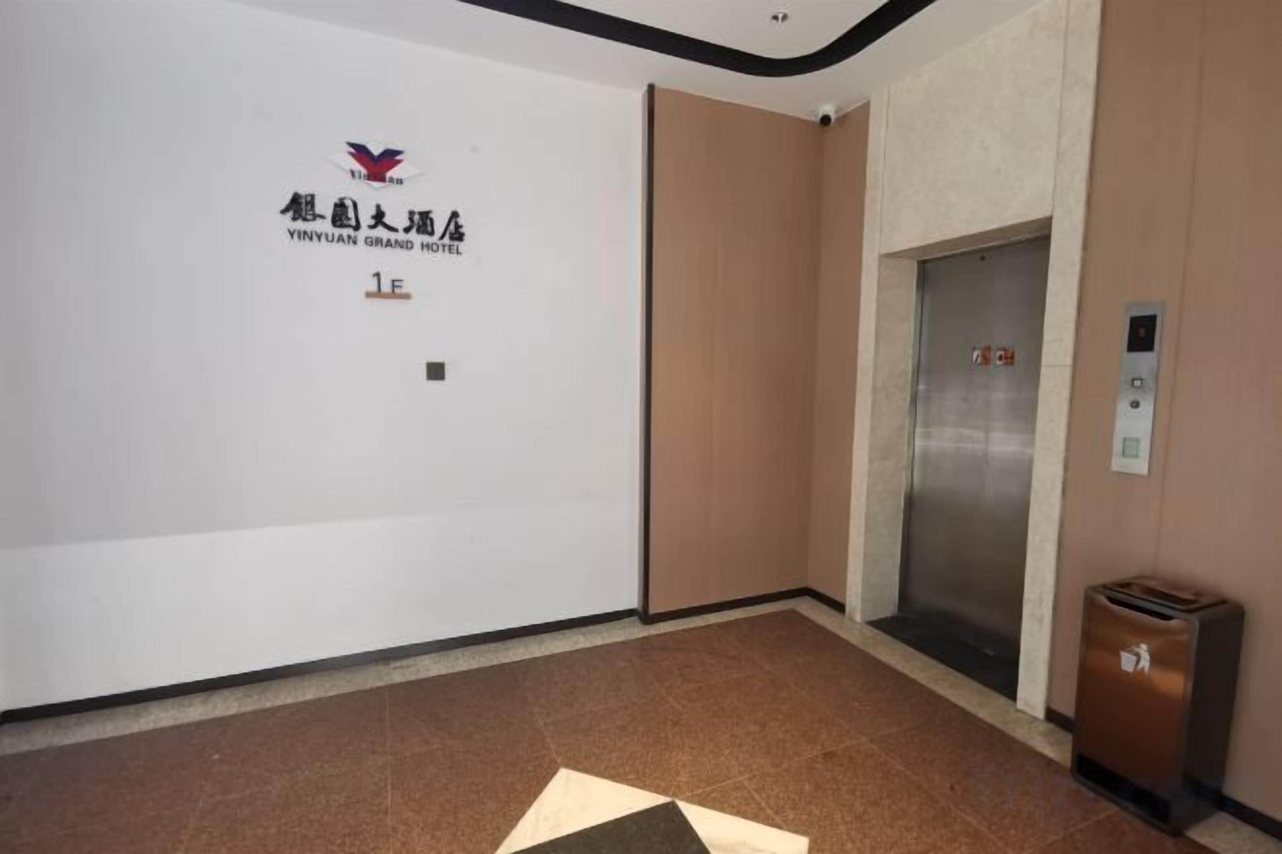 A hotel lobby with a reception desk, an elevator, and a trash bin.