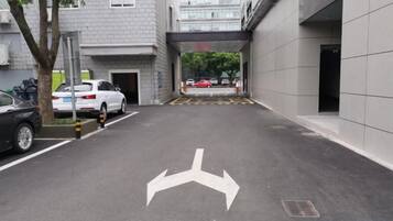 Un área de estacionamiento con flechas direccionales en el suelo, un árbol y la entrada a un edificio.