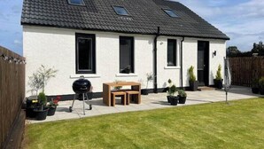A single-story house with a tiled roof, a front door, and a small patio area with a table and chairs. - St Annes - Cosy Cottage in fife (Kirkcaldy)
