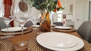 A dining table set with clear wine glasses, white plates, and a decorative vase with green foliage. - St Annes - Cosy Cottage in fife (Kirkcaldy)