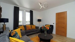 A modern living room with a grey sofa, yellow cushions, a round coffee table, and a wooden door. - St Annes - Cosy Cottage in fife (Kirkcaldy)