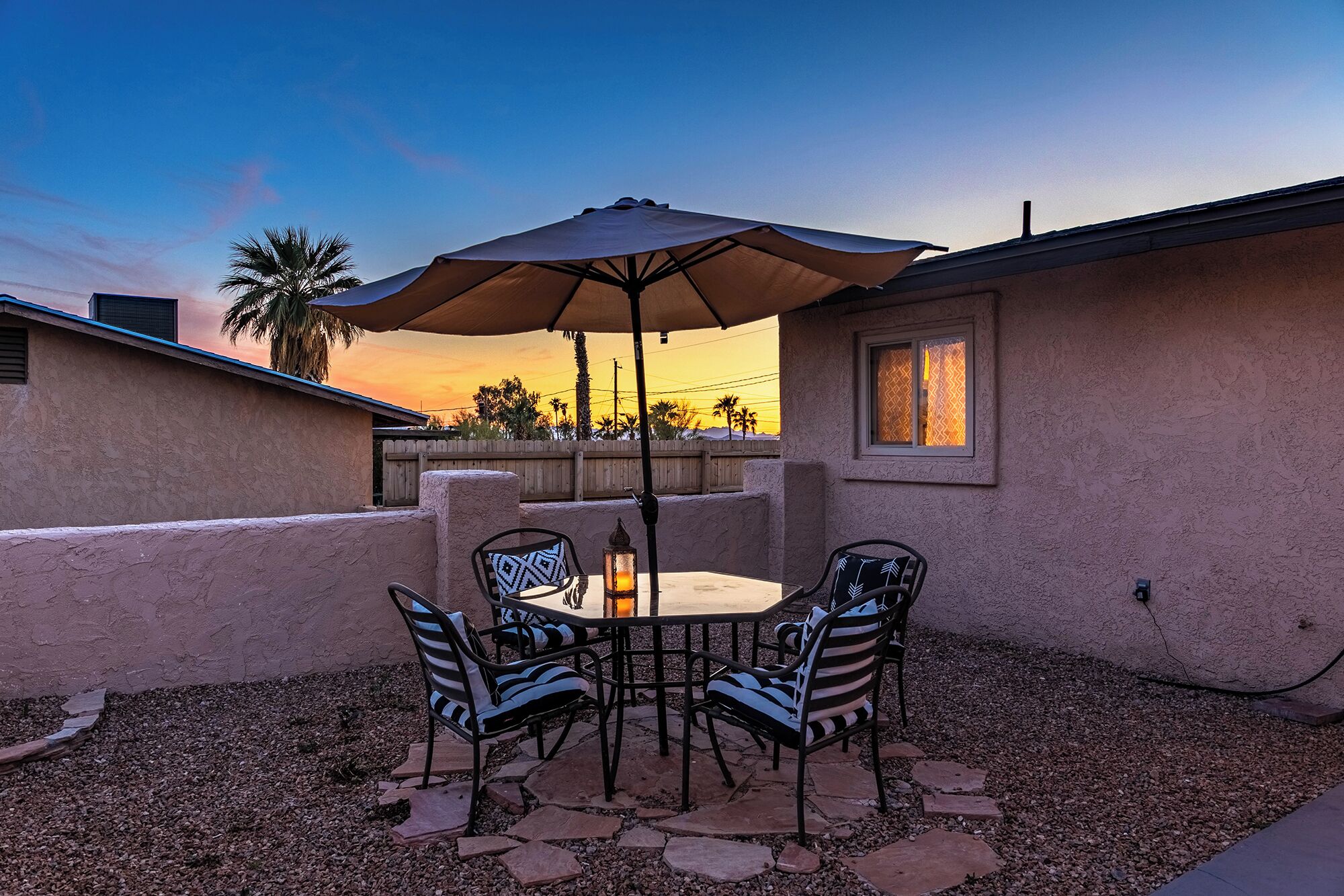 An outdoor patio with a table and chairs, a large umbrella, and a view of the sunset.