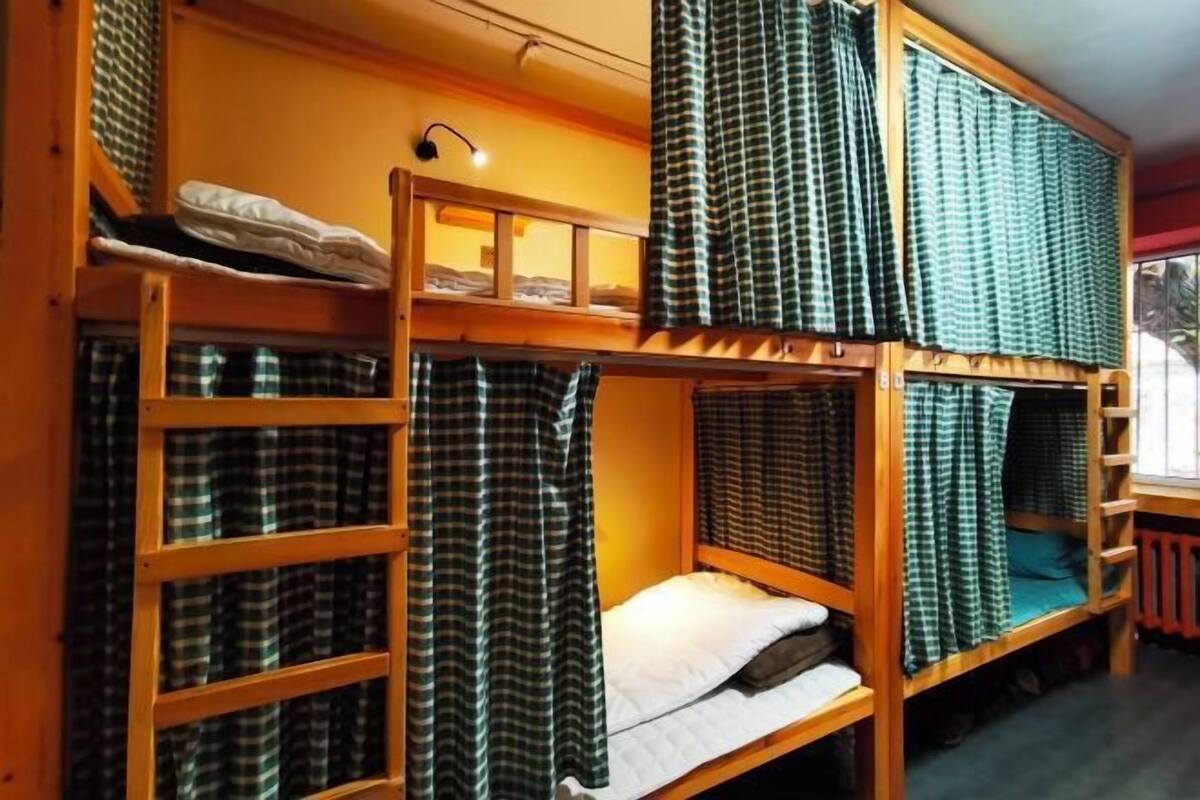 Une chambre avec un lit superposé, des rideaux à carreaux et un petit bureau avec une lampe.