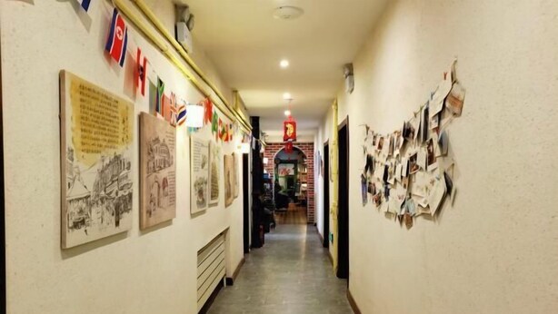 A hallway with framed pictures and flags on the walls, leading to a room with a red sign. - Daoxiang International Youth Hostel(Harbin Central Avenue) (Harbin)