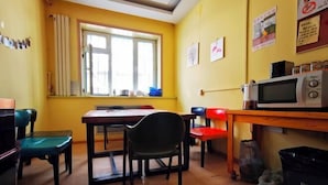 A dining area with a wooden table and chairs, a window with curtains, a microwave, and a trash bin. - Daoxiang International Youth Hostel(Harbin Central Avenue) (Harbin)