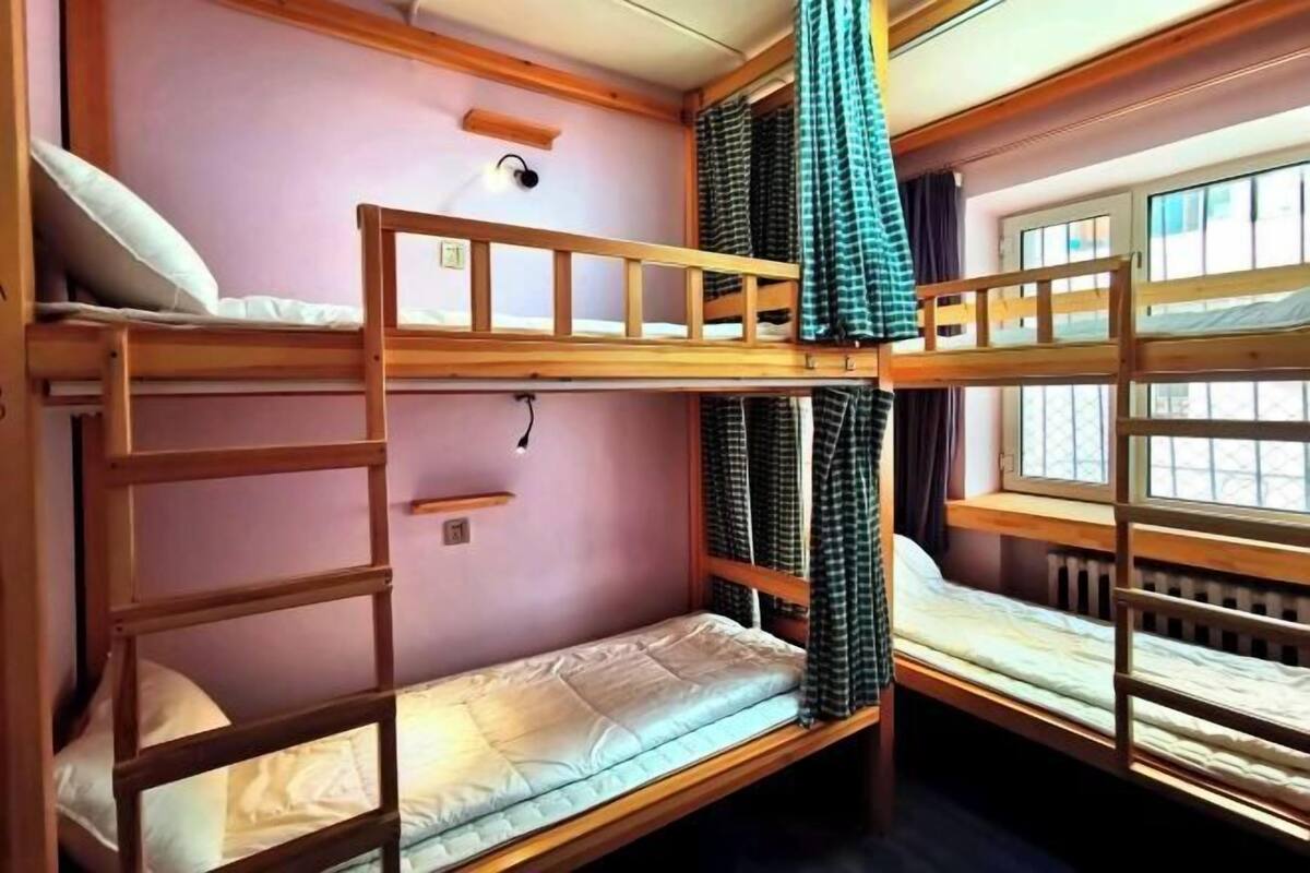 Une chambre avec un lit superposé doté de barrières en bois, une fenêtre avec des rideaux et un luminaire fixé au mur.