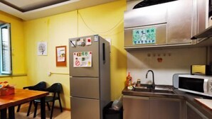 A compact kitchen with a refrigerator, microwave, and sink. There are chairs and a table, and a trash bin is visible. - Daoxiang International Youth Hostel(Harbin Central Avenue) (Harbin)