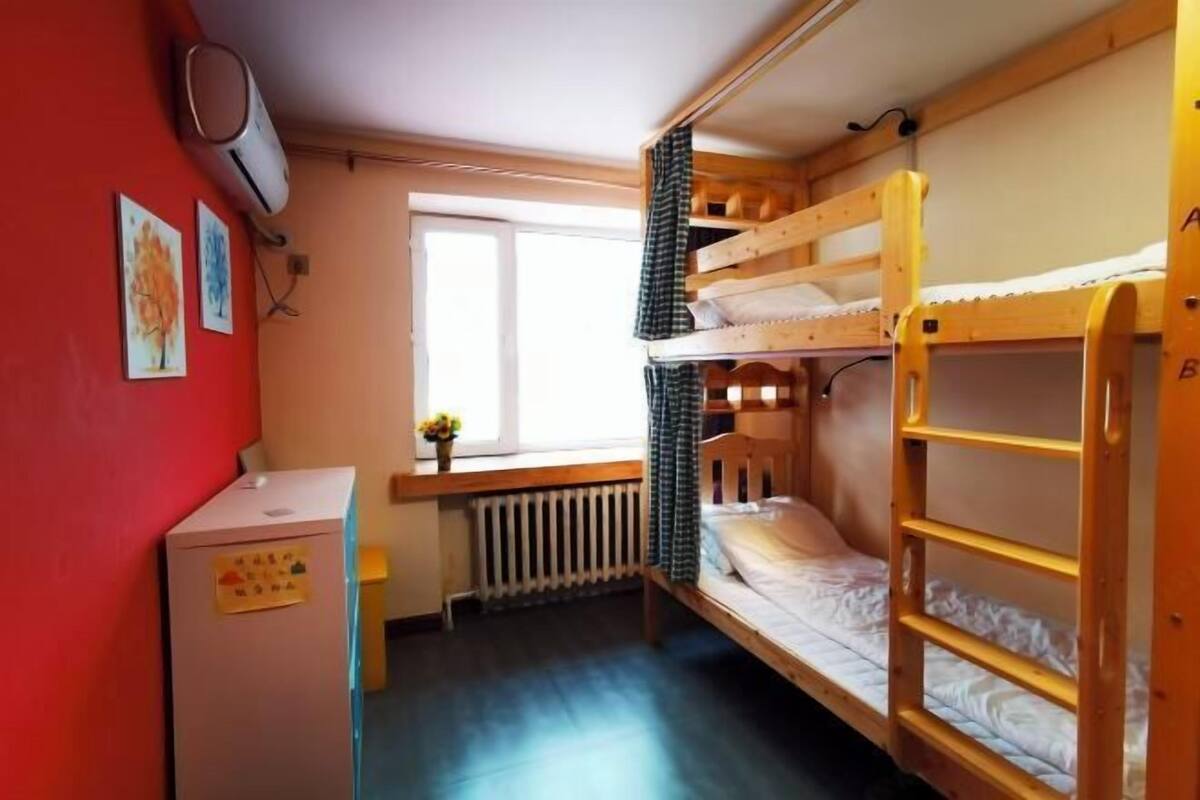 Une chambre de dortoir avec des lits superposés, un bureau, un radiateur et une fenêtre.
