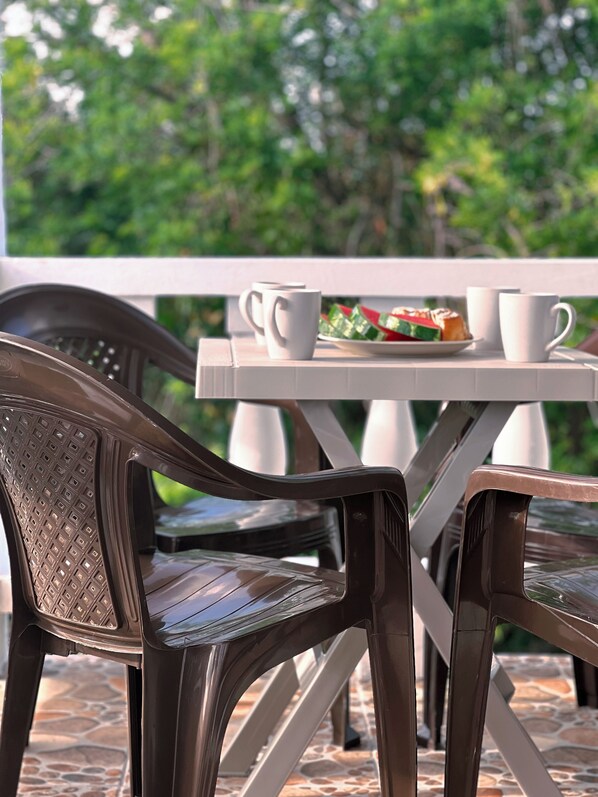 Un patio con dos sillas, una mesa, un plato de comida y una taza blanca.
