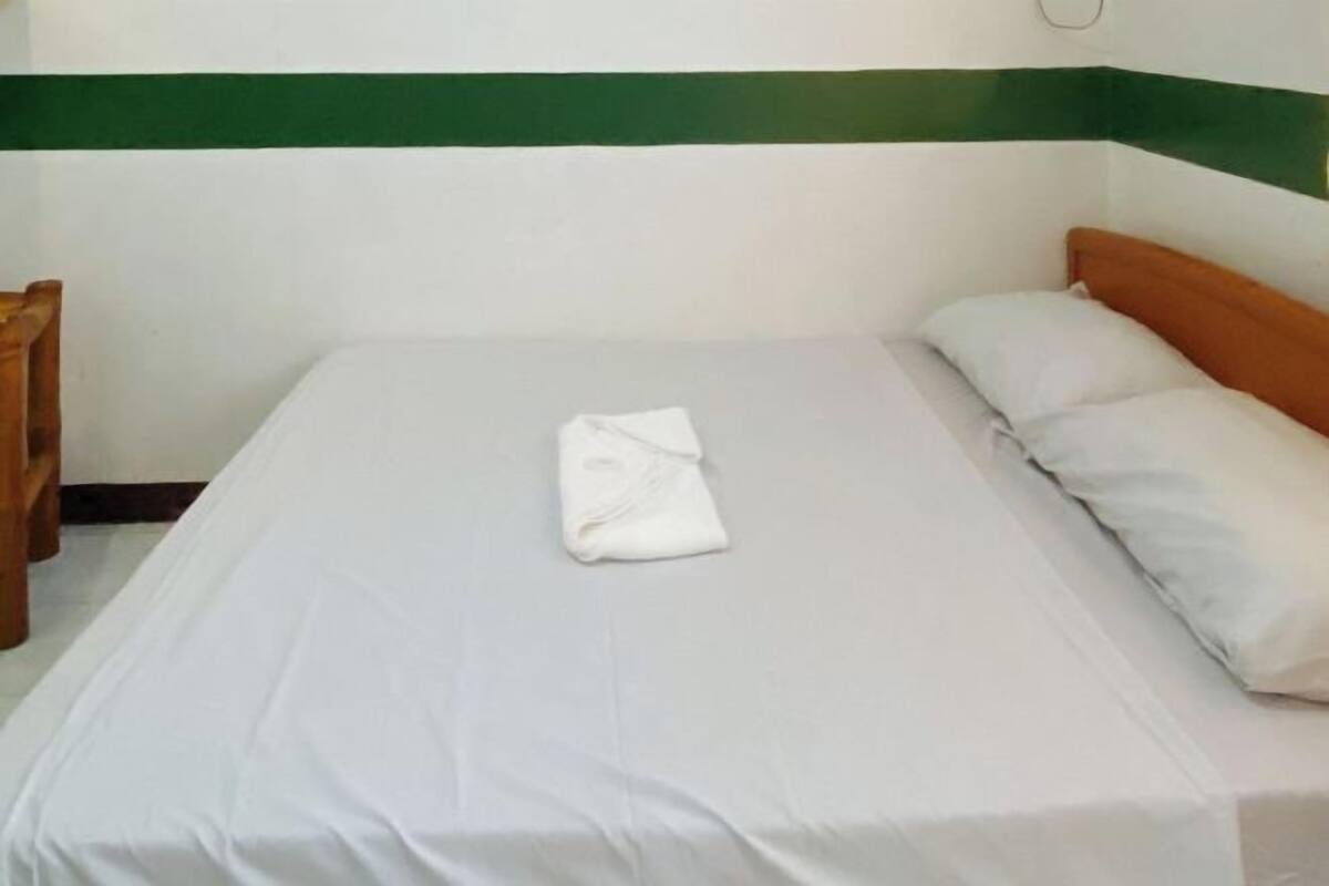 A single bed with white bedding, a folded white towel, and a wooden headboard.