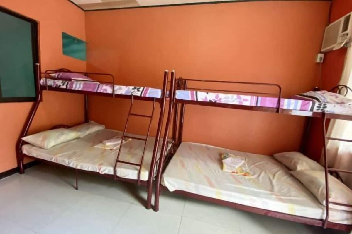 A dormitory room with bunk beds, a greenboard on the wall, and an air conditioning unit.