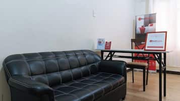 Un canapé en cuir noir, une petite table avec des chaises et une affiche accrochée au mur.